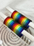 Two rainbow-colored bobbins in a clear plastic case on a white background