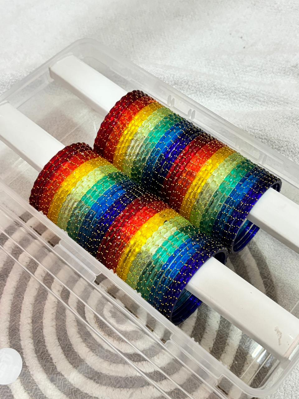 Two rainbow-colored bobbins in a clear plastic case on a white background